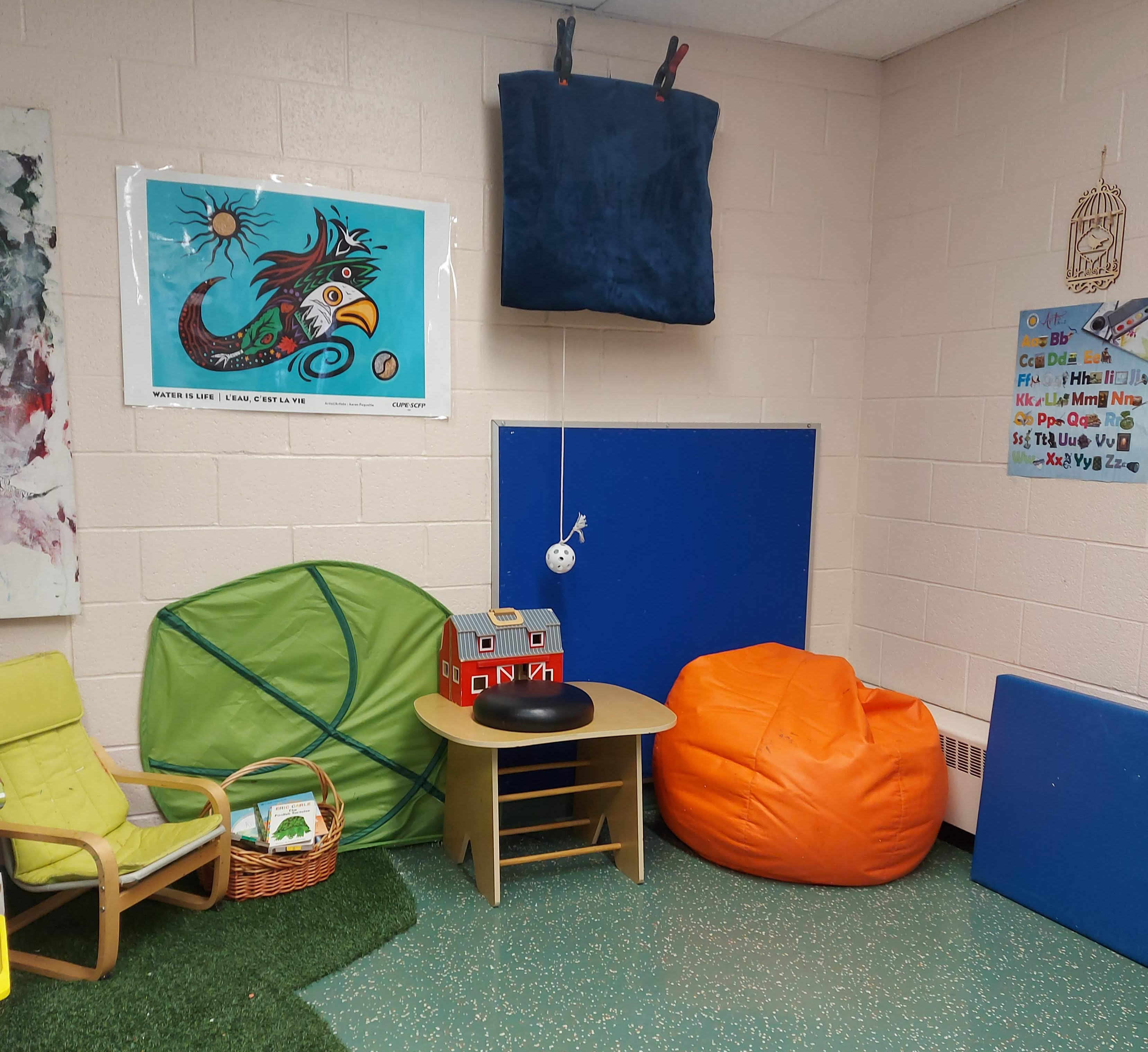 A corner of a classroom with two bean bags for seating, a smal table, a small chair, and some floor mats a couple of different toys