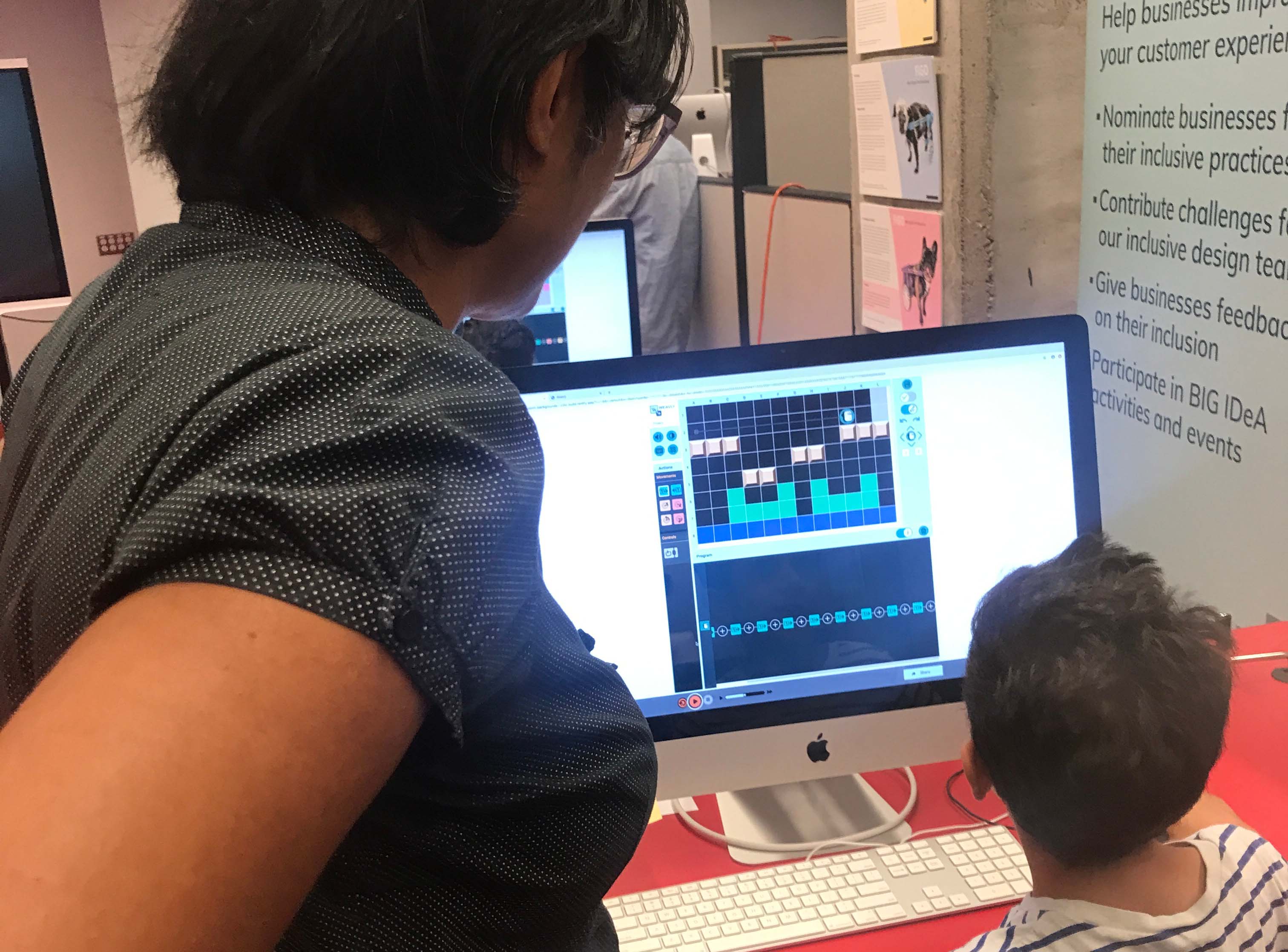 Facilitator observing a child using Weavly coding environment on a computer.