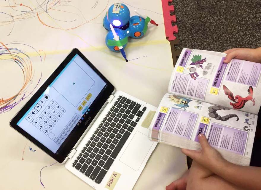 A child using a book, a robot, and a laptop to build a program in Weavly. 